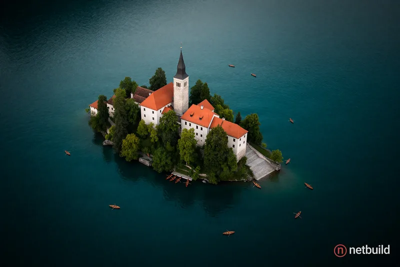 Top-down aerial shot of a small forested island isolated in a vast, deep teal lake. Lush green trees encircle historic …