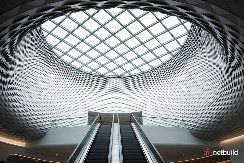 Low-angle shot looking up at a massive circular skylight within a funnel-shaped ceiling, thousands of interlocking white …
